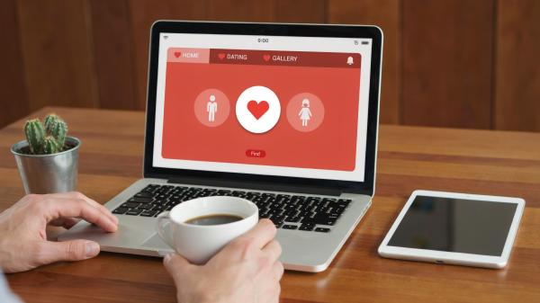 a person drinking coffee and looking at a laptop displaying a dating app