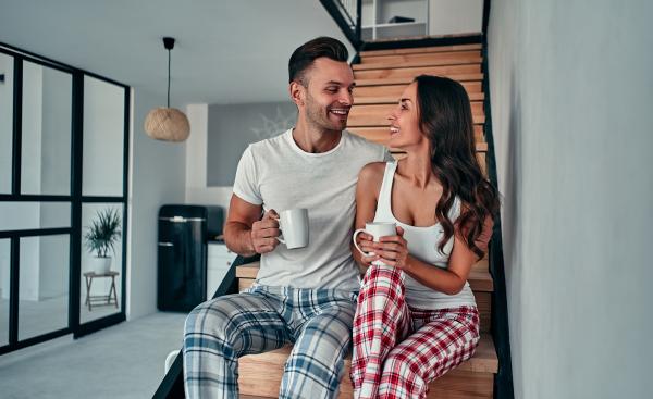 a man and woman sitting on stairs talking in pajamas, each holding a coffee cup