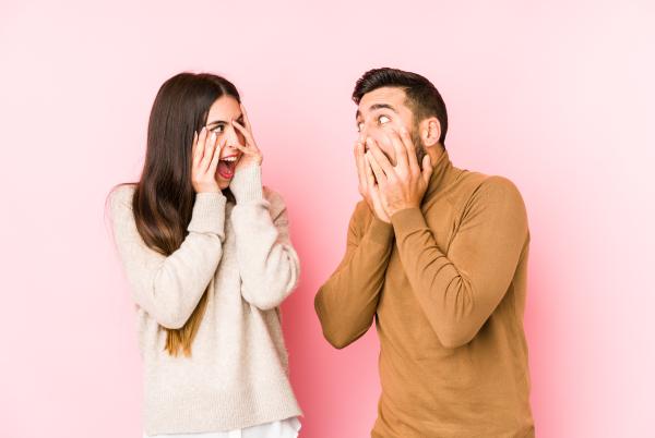 a woman and man covering their faces with their hands in a silly, anxious gesture