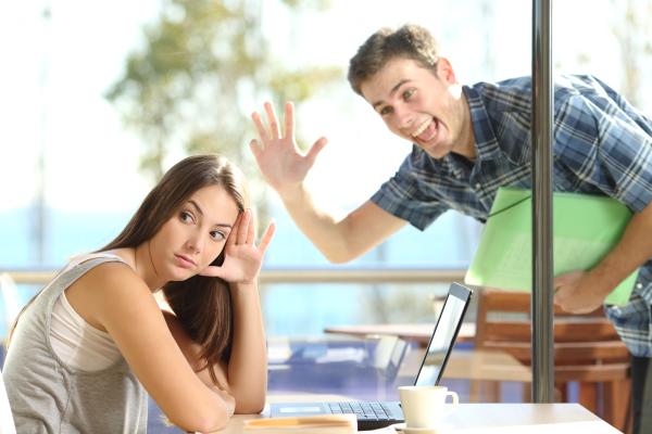 an excited man waving to a woman sitting at a table who is uninterested